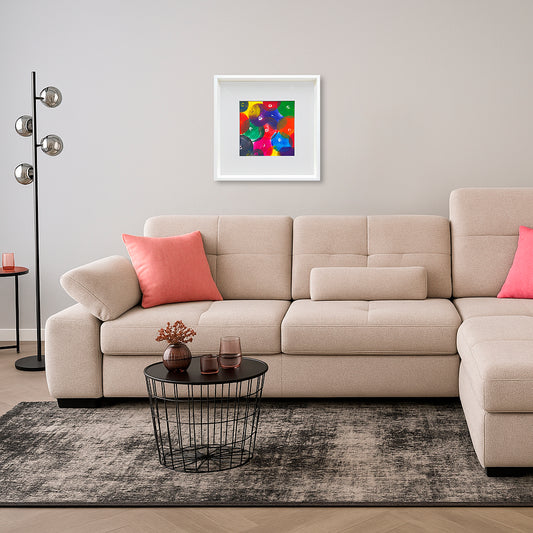 Acrylbild auf Aquarellkarton in einem weißen Holzrahmen mit einem weißen Passepartout an einer weißen Wand. Das Kunstwerk erinnert an ein Bällemeer. Es wurde mit vielen bunten Bruststempeln erzeugt. Darunter befindet sich eine beige helle Wohnlandschaft. Davor ein schwarzer Draht-Couchtisch und links im Bild eine Stehlampe mit 4 Glaskugeln.