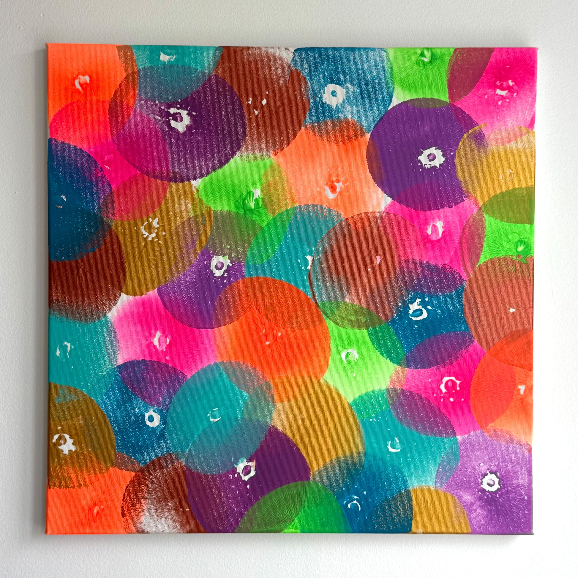 Die frontale Abbildung eines Kunstwerks in der Größe 50x50cm. Acryl auf Leinwand. Das Kunstwerk wurde ausschließlich mit Abdrücken einer Brust erschaffen. Es gibt zahlreiche Abdrücke in 8 verschiedenen Farben. Die Farben sind knallig bis neon, Gold und Kupfer.