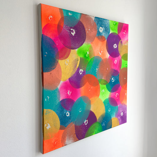Die perspektivische Abbildung eines Kunstwerks in der Größe 50x50cm. Acryl auf Leinwand. Das Kunstwerk wurde ausschließlich mit Abdrücken einer Brust erschaffen. Es gibt zahlreiche Abdrücke in 8 verschiedenen Farben. Die Farben sind knallig bis neon, Gold und Kupfer.